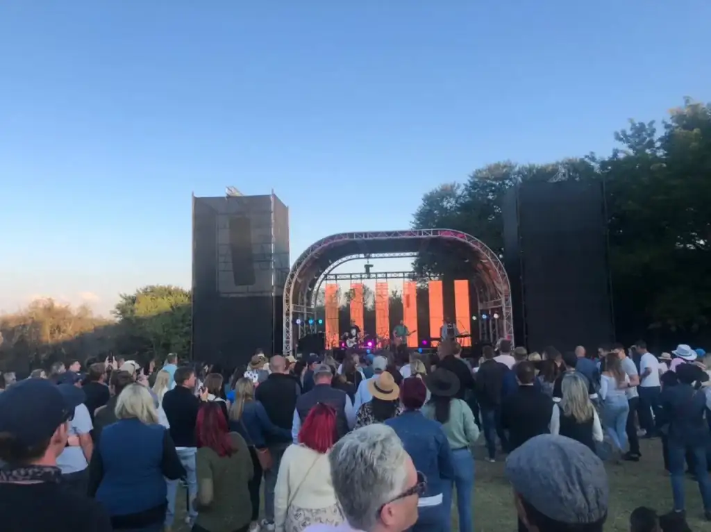 Outdoor festival stage with line-array speaker towers and a big crowd at sunset
