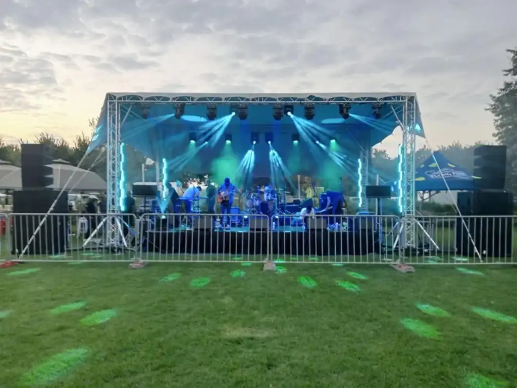 Truss stage with blue and green lighting and a band playing on grass